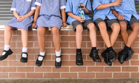 The legs and feet of schoolchildren sitting on a wall