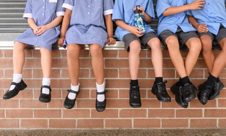 School children sit on a brick wall with their legs dangling over the top.