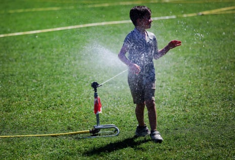 A young boy cools off at a grass sprinkler on a hot summer day at Parliament Square in London