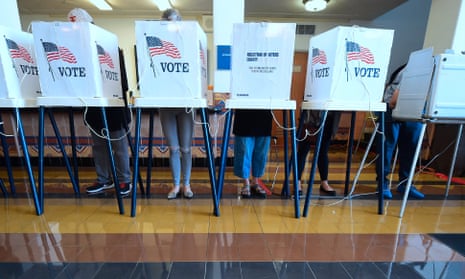 Five people, their upper bodies concealed by white voting booth partitions with the word "VOTE" printed on them, fill out ballots at a polling site in California.