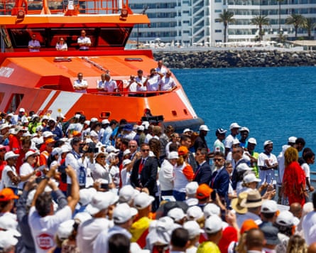 People on the dock and on a docked large orange vessel