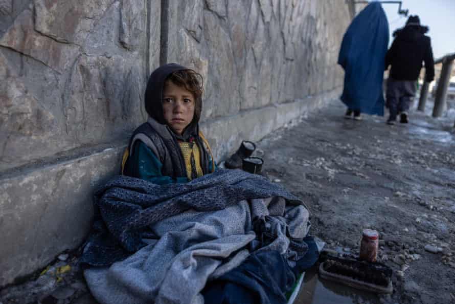 a small girl sits on a snowy pavement with brushes and shoe polish in front of her