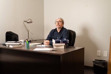 man in navy button-down shirt sits at desk with hands folded