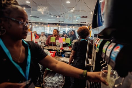 woman fills up drink at soda machine as customers stand by counter behind her