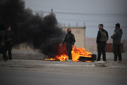 Three people standing near tyres burning on the ground, giving off thick black smoke