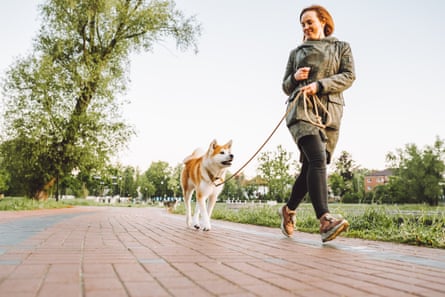 Woman running with her dog in the public park along a lake early in the morning
