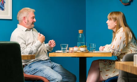 A man and a woman sitting talking at a restaurant table in front of a blue wall