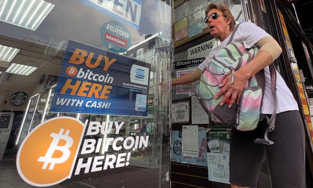 A woman carrying a backpack leaves a convenience store that has signs in the window announcing 'Buy bitcoin here!'