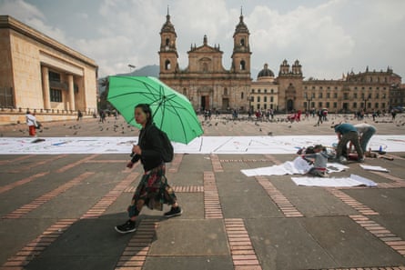 A woman with parasol walks past a large white banner spread out in a city square