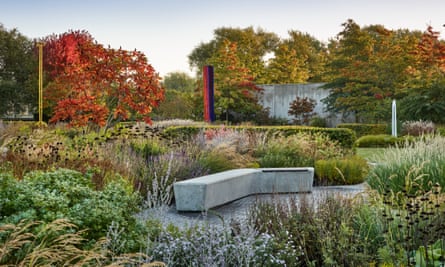 contemporary garden with seating in the foreground and planting with sculptures in the background