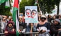 A crowd of people on a pro-Palestine march stand behind barriers and hold flags and banners