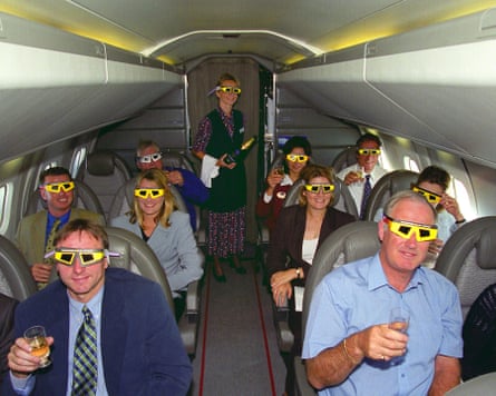 Passengers in a plane holding glasses of champagne and wearing special eclipse-viewing glasses
