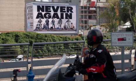 A motorcyclist rides past a billboard depicting the leaders of Hamas on their knees as prisoners under the words ‘Never again’