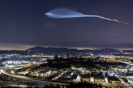 A light trail across the evening sky above the lights of a city