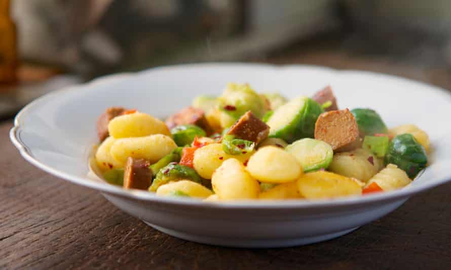 Plate with gnocchi, served with Brussel sprouts and vegan hot dog pieces.