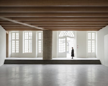 A figure walks through a doorway in Design Museum Ghent’s room with wooden beamed ceiling and tall windows