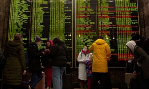 People stand in front of the train schedule at Central Railway Station as they try to leave Kyiv.