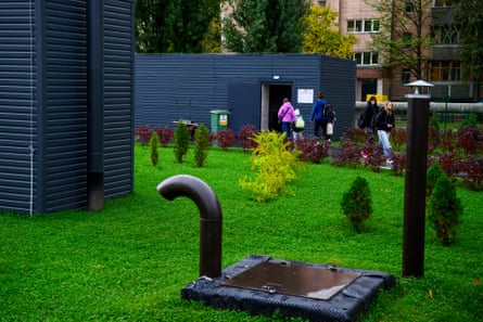 People leave an underground school’s entrance building, crossing a lawn with shrubs