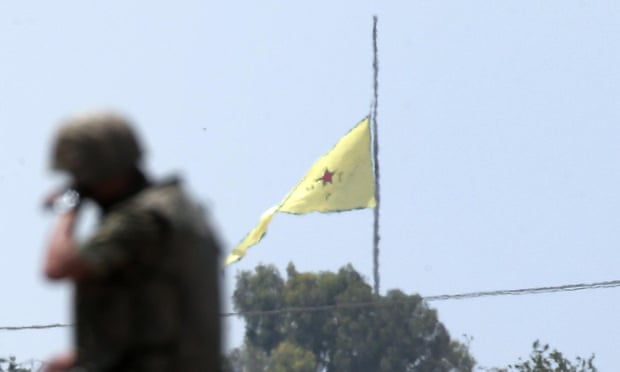 A Turkish soldier stands on an armoured personnel carrier as in the background a flag of the Kurdish YPG units is raised over the town of Tal Abyad, Syria, on Tuesday.