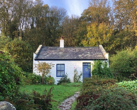 A whitewashed cottage with blue door and window frame set in a garden with lawn, shrubs and winding gravel path