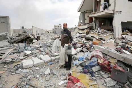 A view of the area after an alleged Israeli air strike hit an apartment belonging to the al-Tababi family in Nuseirat on Friday evening. A man stands among rubble holding clothes and a small grey plastic basket.