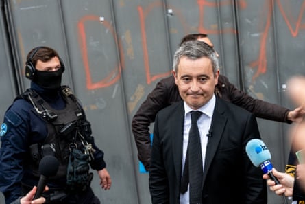 Darmanin being interviewed in front of a corrugated metal wall with letters spraypainted on it