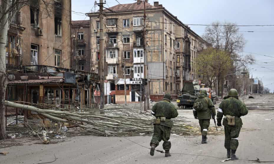 soldiers walk past damaged buildings