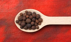 Allspice (Pimenta dioica) berries on wooden spoon over red painted textile background<br>J0MGT2 Allspice (Pimenta dioica) berries on wooden spoon over red painted textile background