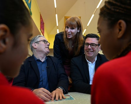 Rayner stands between a seated Starmer and Burnham as they face school pupils