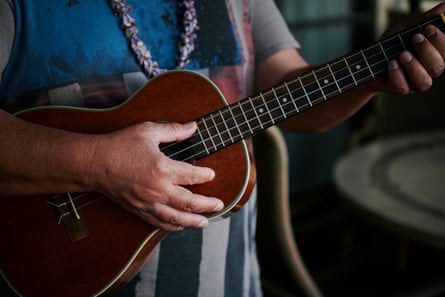 A close-up of two hands playing a glossy brown ukulele.