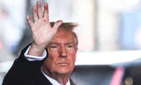 White man wearing suit raises his hand.