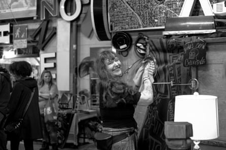 A black-and-white image of a smiling woman in a black T-shirt, jeans, and fanny pack hanging something on a wall.