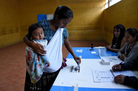 An indigenous woman holding a baby casts her vote during runoff elections in Santa Cruz Chinautla, Guatemala,