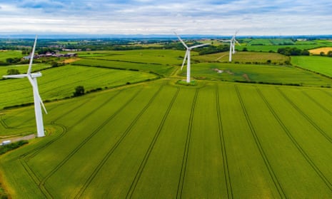 wind turbines stretch across lush green farmland