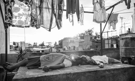 A scene from Roma of a young girl and boy lying on a Mexico City rooftoop amid laundry hanging on lines and the sun breaking through.