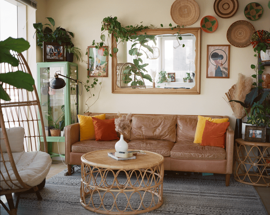 A view of a living room with a brown leather couch, rattan furniture, and plants