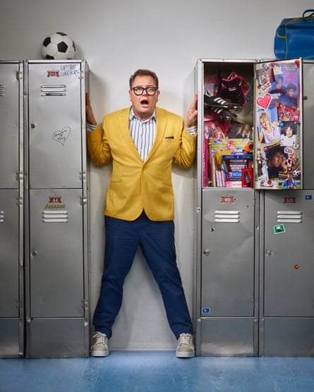 Alan Carr photographed against school lockers with 80s-style posters and gear