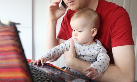 A father works on his laptop from home while holding his eight month old baby.