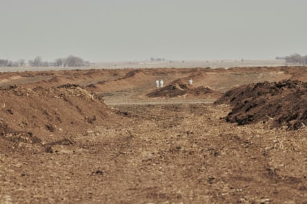 Two figures in white protective suits are seen in the distance amid mounds of bare soil