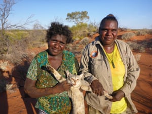 Pintupi women Yukultji Napangarti and Christine Michaels display a dead feral cat which was caught by the Kiwirrkurra community.