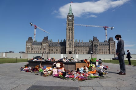 Justin Trudeau next to a collection of floral tributes with the Canadian parliament building in the background