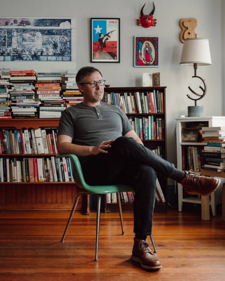 man seated with legs crossed in front of bookshelf