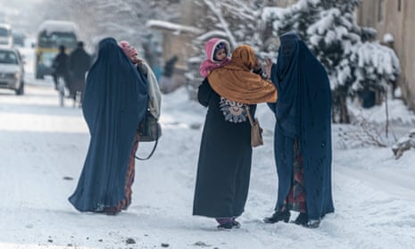 Afghan burqa-clad women carry children as they walk in the snow in Kabul on January 23, 2023. 