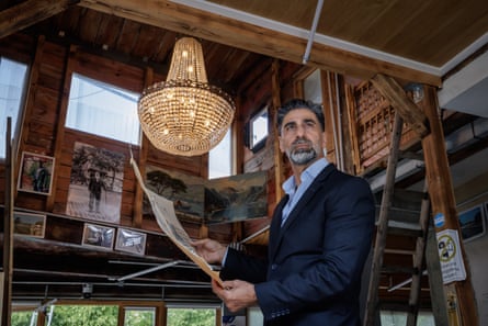 Suat Özkan inside the wooden treehouse. An ornate chandelier-style light fitting dangles behind him and there are photos on the walls.