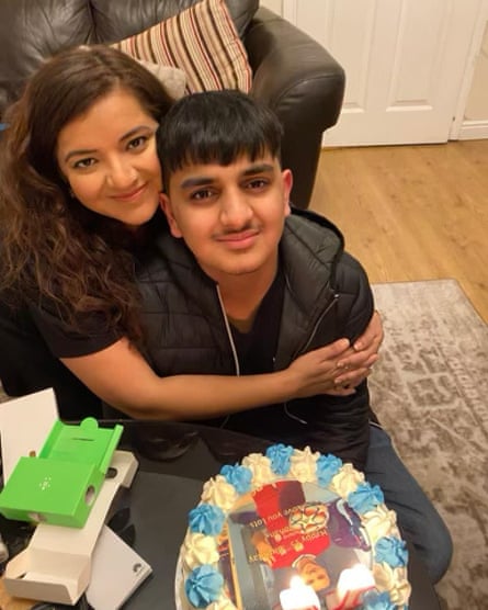 Pooja and Ronan Kanda in front of a birthday cake with blue and cream icing and lit candles; she has her arms around her son and they are both smiling