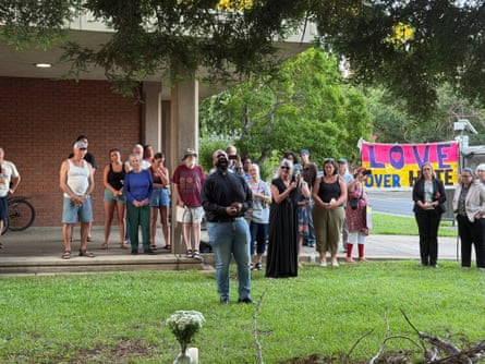 people stand outside next to a sign saying ‘love over hate’ at vigil