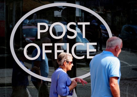 Two people walk past a large Post Office logo