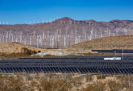 solar panels in foreground, wind turbines in background in desert