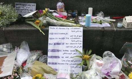 A sign, in Arabic and English, is placed before flowers at a memorial in Potters Field Park, London.