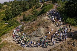 Hundreds of people walk along a path snaking down a scrubby hill